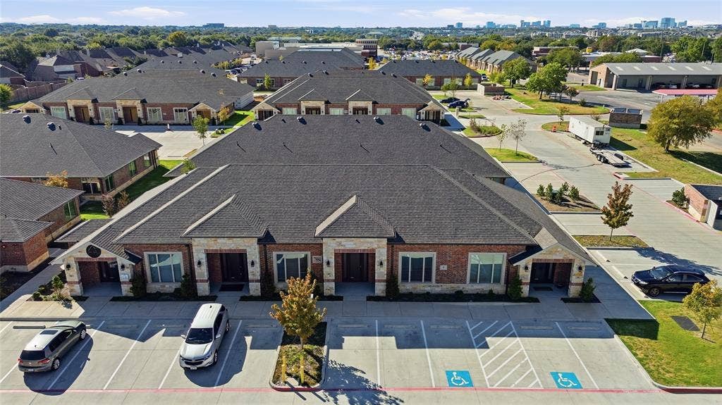 Brick and masonry exterior featuring shingle roofing, paved surface parking, and exterior lighting fixtures