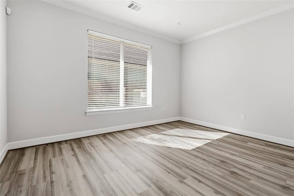 Neutral-toned interior featuring wood-finish flooring, crown molding, and a large window with fitted blinds