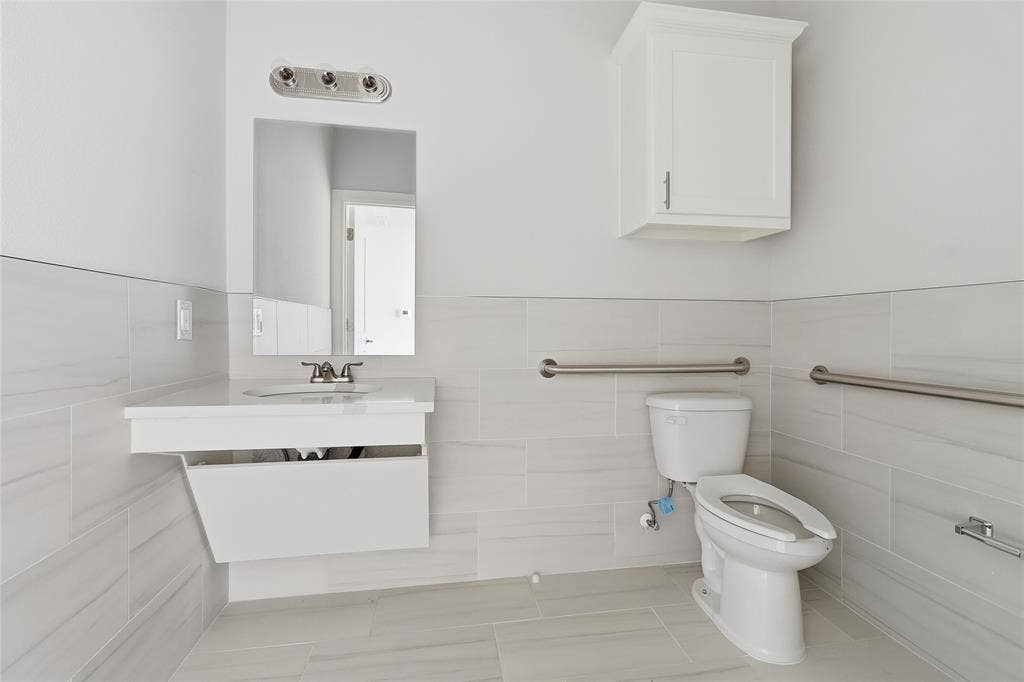 Wall-mounted vanity with rectangular sink, white wall cabinet, horizontal tile wainscoting, and stainless steel grab bars