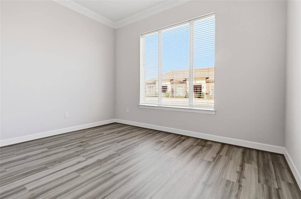 Neutral-toned interior space featuring wood-finish flooring, crown molding, and a multi-panel window