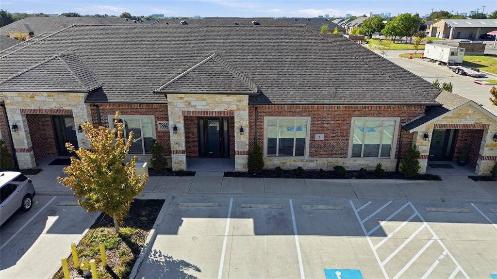 Multi-tenant building featuring brick and stone masonry, multi-gabled roofline, concrete parking area, and manicured foundation landscaping