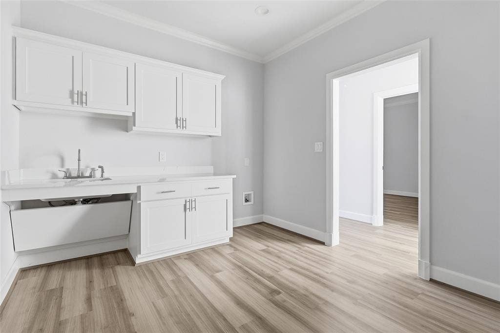 White cabinetry featuring brushed nickel hardware, stone-finish countertops, integrated sink, and wood-finish flooring