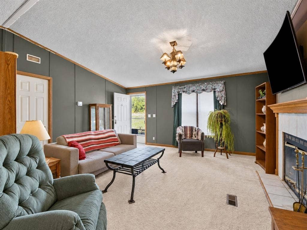 1528 CR 697, Farmersville, TX 75442 Vaulted ceilings, fireplace with tile surround and wood mantel, built-in shelving, multi-arm light fixture, and neutral carpeting