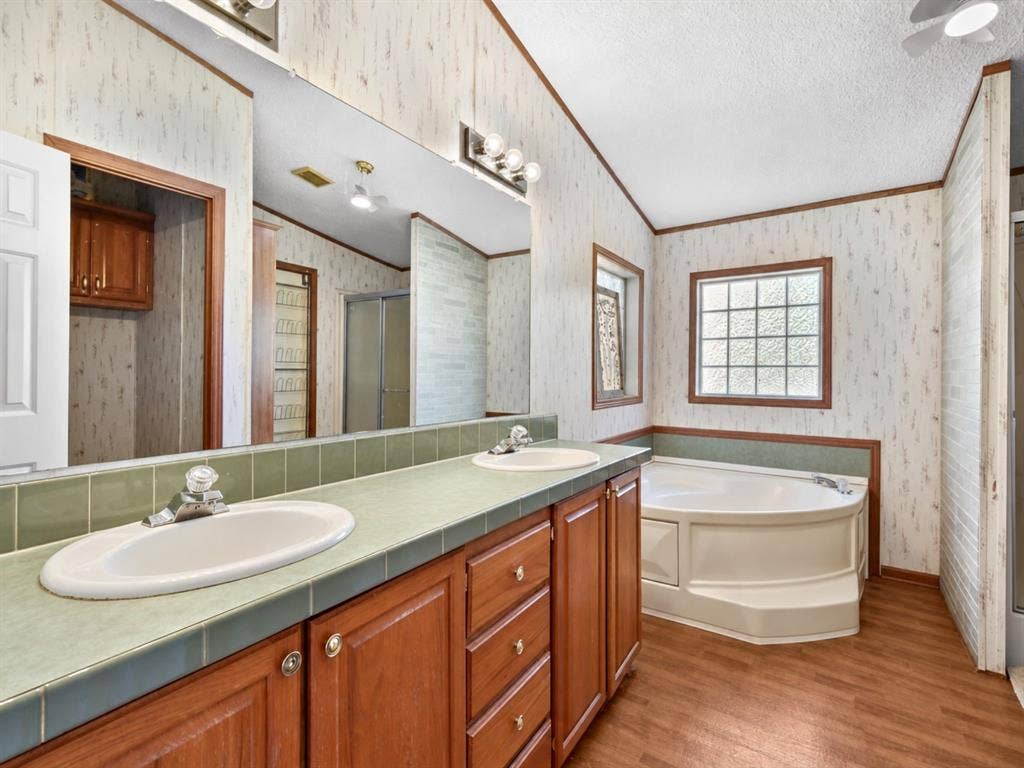1528 CR 697, Farmersville, TX 75442 Dual-sink vanity with tile countertop, wood-finish cabinetry, corner soaking tub, and block-pattern privacy window