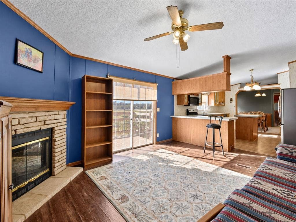 1528 CR 697, Farmersville, TX 75442 Stone fireplace with wood mantel, built-in shelving, sliding glass door, wood-finish flooring, and peninsula kitchen counter