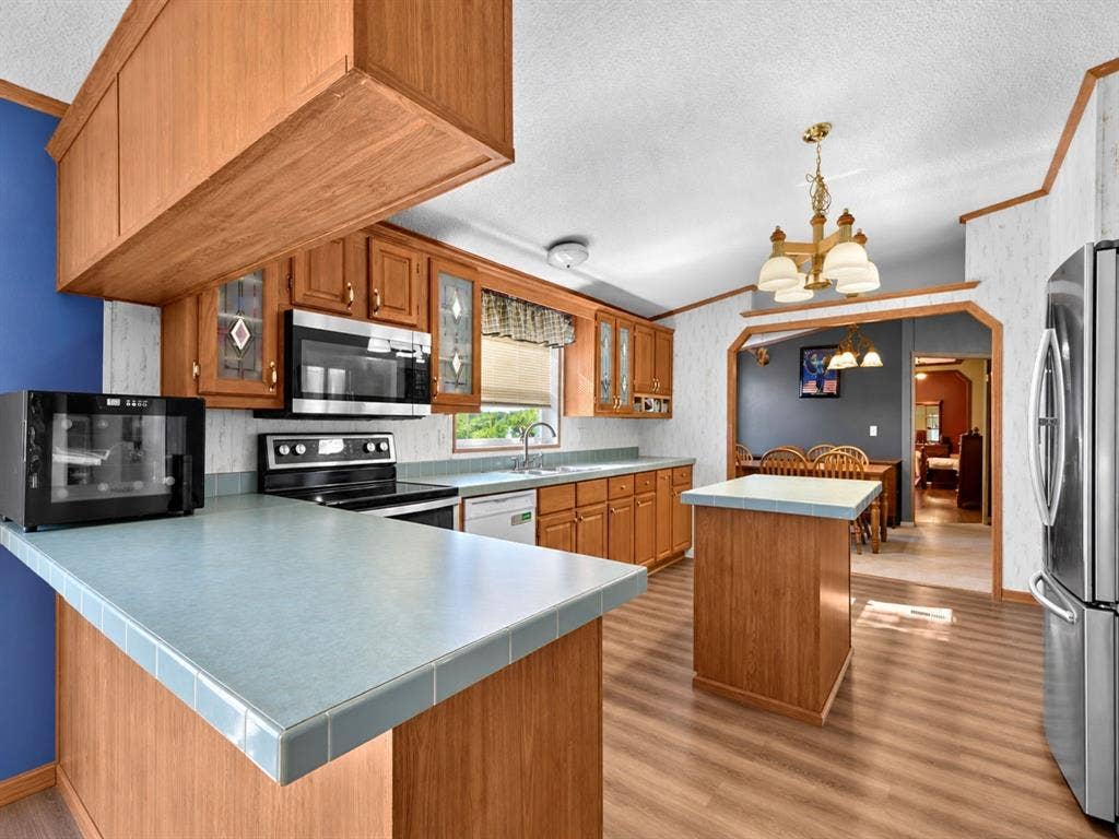 1528 CR 697, Farmersville, TX 75442 Kitchen featuring wood cabinetry, tiled countertops, stainless steel appliances, a center island, and wood-finish flooring