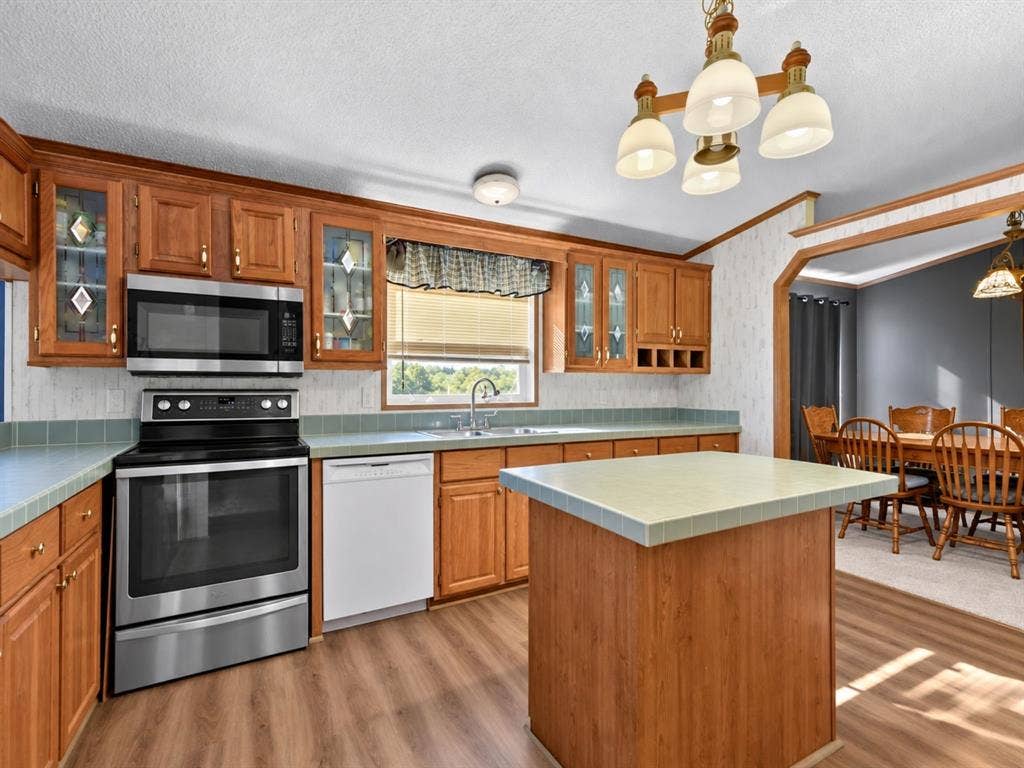 1528 CR 697, Farmersville, TX 75442 Kitchen featuring wood cabinetry, stainless steel appliances, tile countertops, a central island, and wood-finish flooring