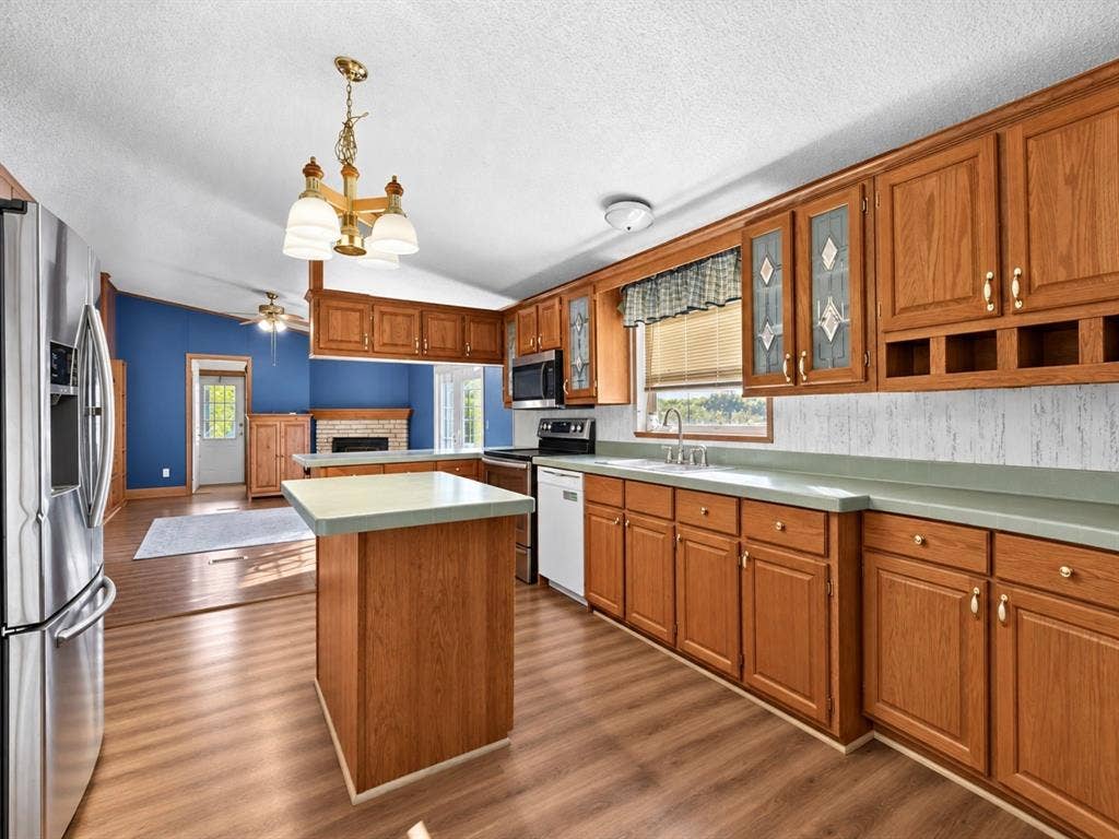 1528 CR 697, Farmersville, TX 75442 Kitchen featuring wood cabinetry, solid surface countertops, an integrated center island, stainless steel refrigerator, and wood-finish flooring