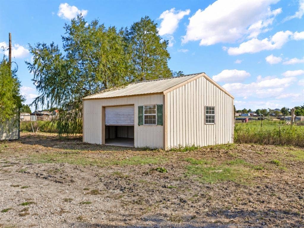 1528 CR 697, Farmersville, TX 75442 Detached metal-sided structure featuring a metal roof, roll-up garage door, and two shuttered windows