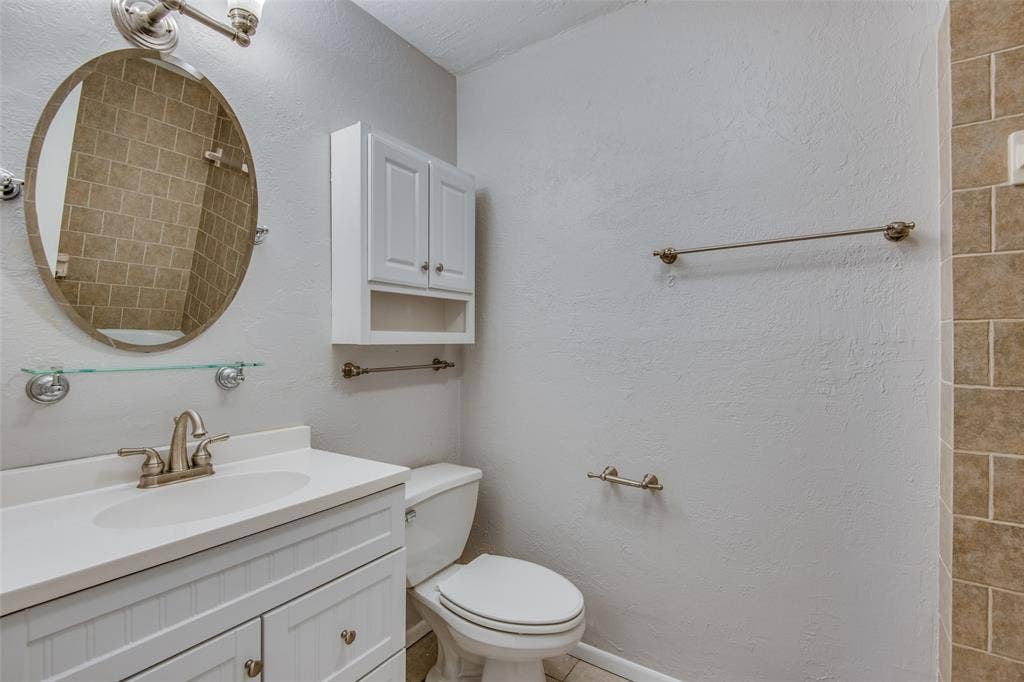 2131 Onetta Drive, Irving, TX 75061 Bathroom featuring a white vanity cabinet with an integrated basin, oval wall mirror, wall-mounted medicine cabinet, and tiled shower surround
