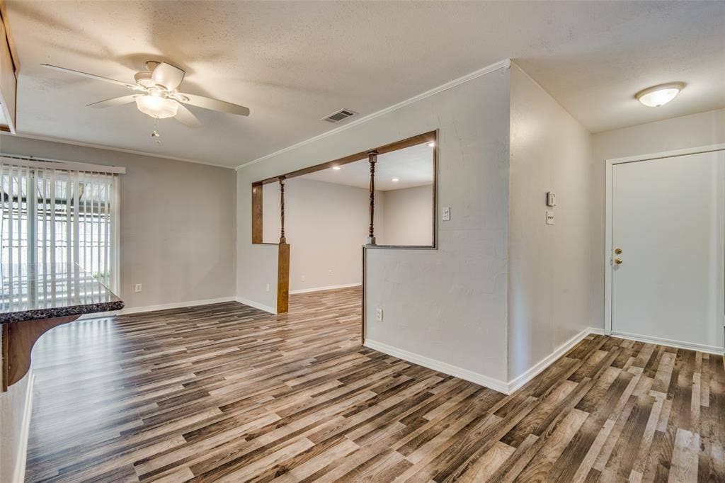 2131 Onetta Drive, Irving, TX 75061 Interior space featuring wood-finish flooring, a ceiling fan with integrated lighting, recessed wall opening with decorative columns, and vertical blinds