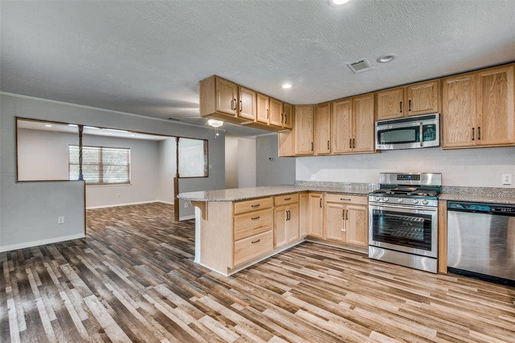 2131 Onetta Drive, Irving, TX 75061 Kitchen featuring natural wood-finish cabinetry, stone-style countertops, stainless steel appliances, recessed lighting, and wood-finish flooring