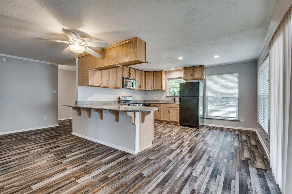 2131 Onetta Drive, Irving, TX 75061 Kitchen featuring light wood-finish cabinetry, stone-composite countertops, wood-finish flooring, a breakfast bar, and a ceiling fan