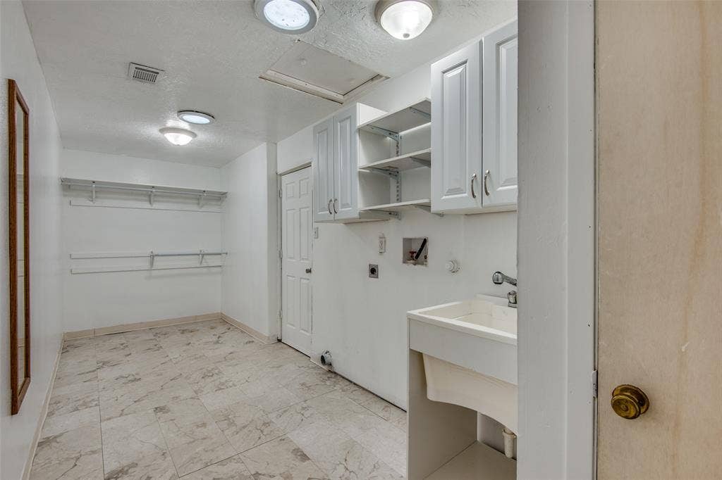 2131 Onetta Drive, Irving, TX 75061 Laundry room featuring stone-finish tile flooring, white cabinetry with open shelving, a utility sink, and wall-mounted storage racks