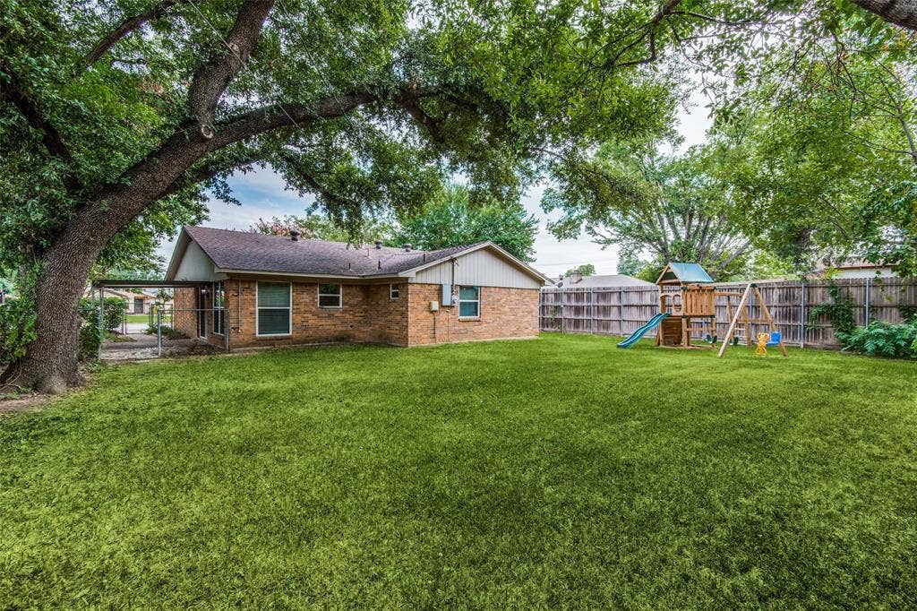 2131 Onetta Drive, Irving, TX 75061 Expansive backyard featuring a manicured lawn, mature trees, wood privacy fencing, and a covered patio area
