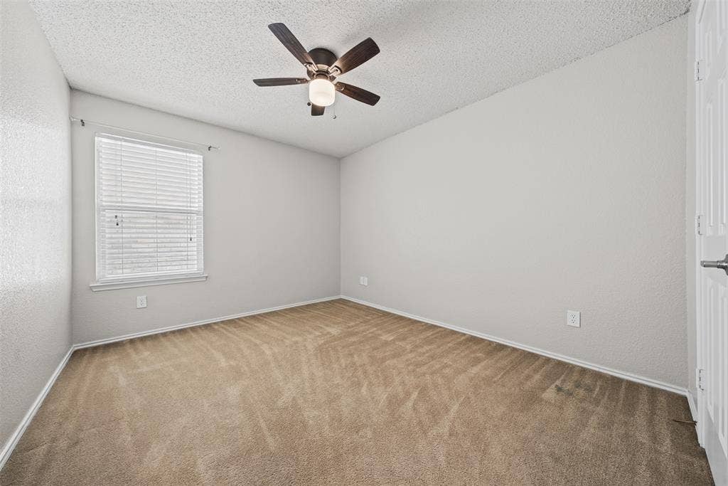 5428 Maverick Drive, Grand Prairie, TX 75052 Neutral-toned interior featuring wall-to-wall carpeting, a multi-blade ceiling fan with integrated lighting, and a single-hung window with horizontal blinds