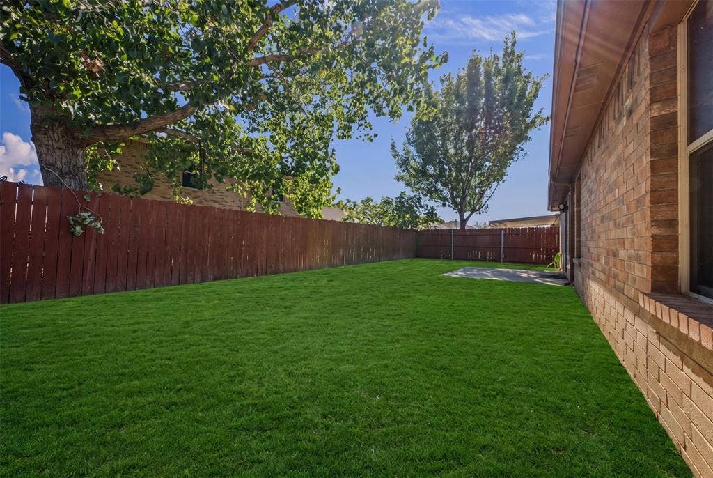 5428 Maverick Drive, Grand Prairie, TX 75052 Private backyard featuring brick exterior siding, a level grass lawn, perimeter wood fencing, and mature trees