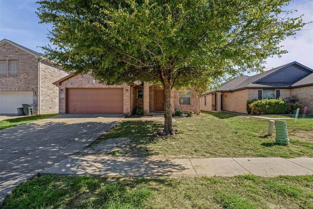 5428 Maverick Drive, Grand Prairie, TX 75052 Brick exterior featuring an attached two-car garage, concrete driveway, and front-facing mature tree