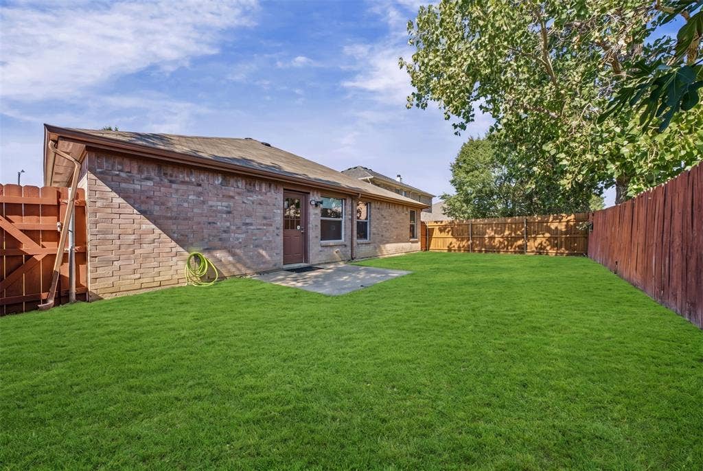 5428 Maverick Drive, Grand Prairie, TX 75052 Rear exterior featuring brick siding, a concrete patio, and a fully enclosed wood fence surrounding a grass lawn