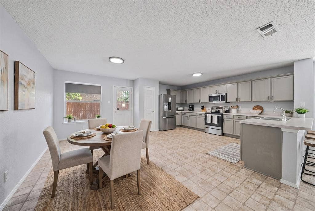 5428 Maverick Drive, Grand Prairie, TX 75052 Kitchen featuring grey shaker-style cabinetry, a central island with an integrated stainless steel sink, tile flooring, and stainless steel appliances