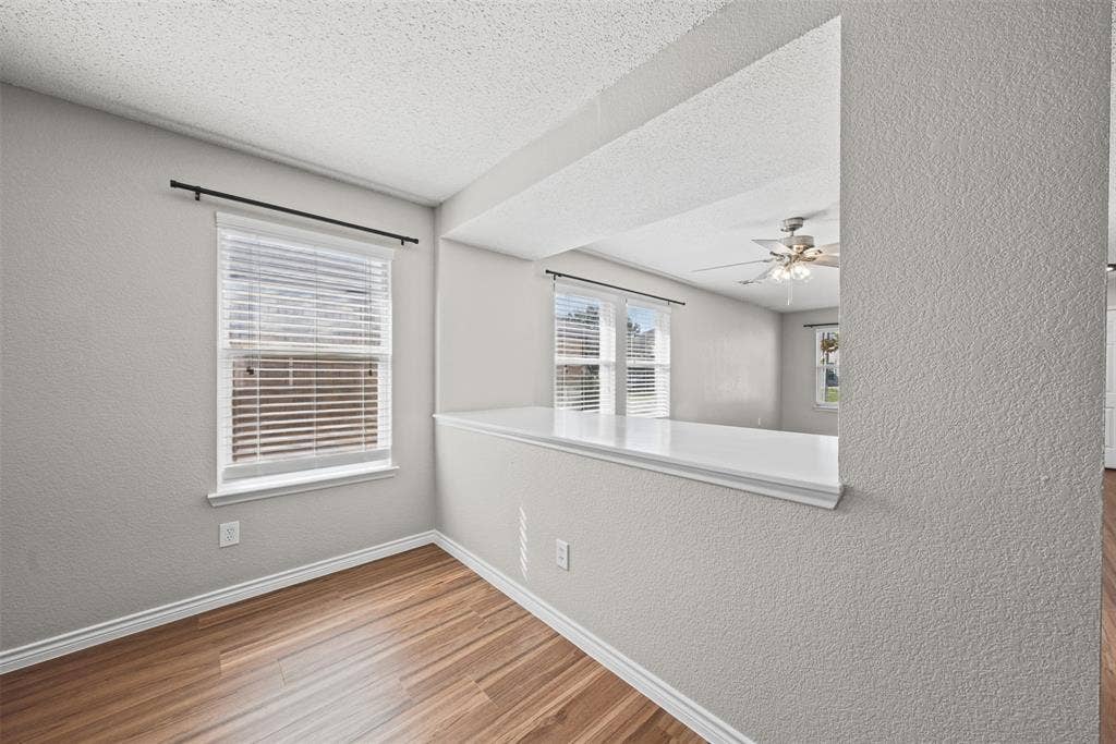 5428 Maverick Drive, Grand Prairie, TX 75052 Wood-finish flooring, neutral textured walls, white-capped pass-through ledge, and windows with horizontal blinds