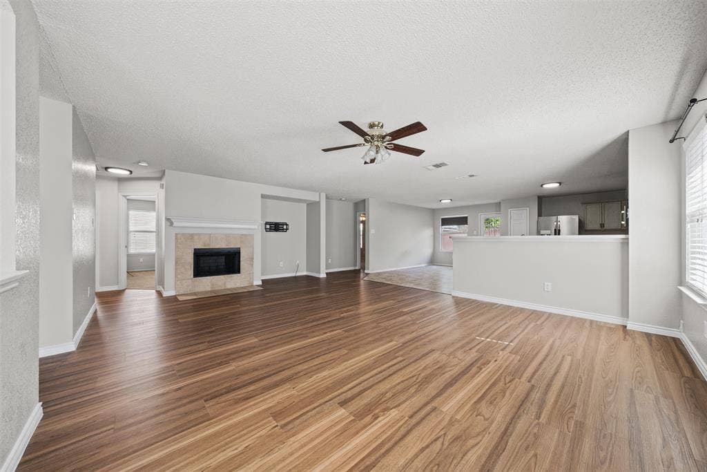 5428 Maverick Drive, Grand Prairie, TX 75052 Open interior featuring wood-finish flooring, a tile-surround fireplace, a ceiling fan with integrated lighting, and a kitchen pass-through counter