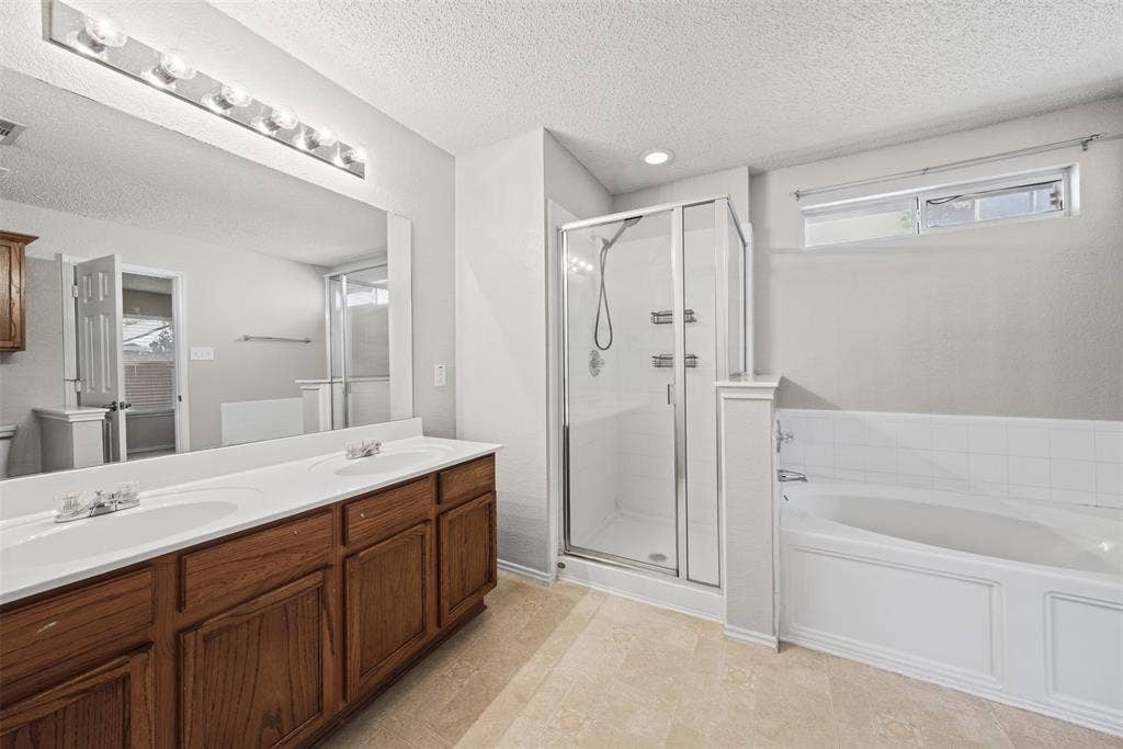 5428 Maverick Drive, Grand Prairie, TX 75052 Bathroom featuring a wood-finish double vanity with dual undermount sinks, a large wall-mounted mirror, a separate glass-enclosed shower, and a soaking tub with tiled surround