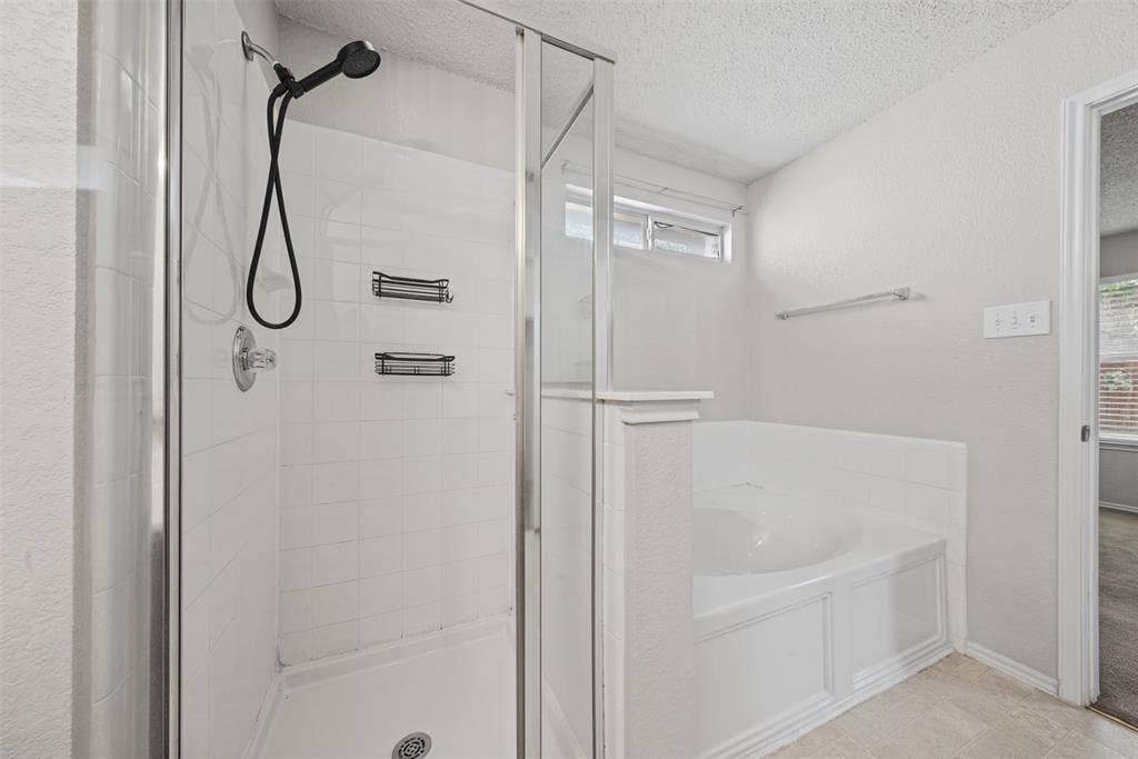 5428 Maverick Drive, Grand Prairie, TX 75052 Walk-in shower with a glass enclosure, matte black rainfall shower head, white tile surround, built-in recessed shelving, and a separate soaking tub with a tiled apron front