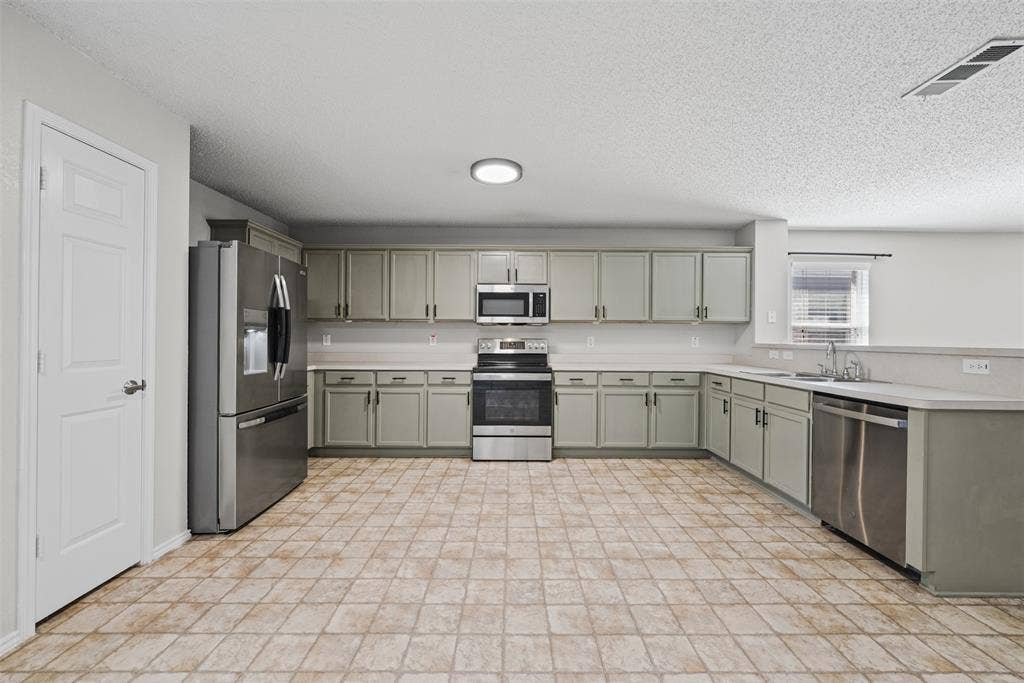 5428 Maverick Drive, Grand Prairie, TX 75052 Kitchen featuring light-toned cabinetry, stainless steel appliances, ceramic tile flooring, and a peninsula with a stainless steel sink