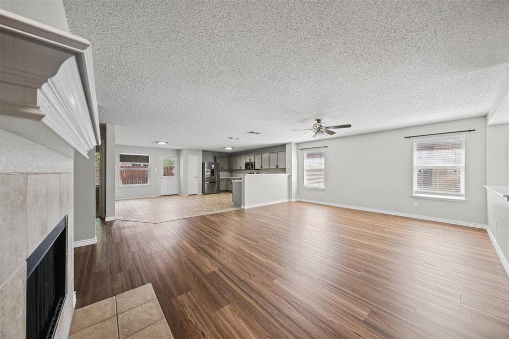 5428 Maverick Drive, Grand Prairie, TX 75052 Open-concept interior featuring wood-finish flooring, a tile-surround fireplace with a mantel, stainless steel kitchen appliances, and multiple windows