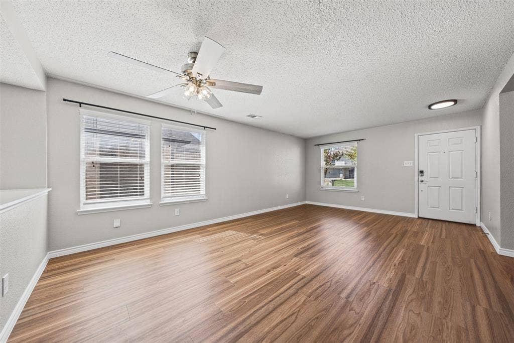 5428 Maverick Drive, Grand Prairie, TX 75052 Spacious room featuring wood-finish flooring, ceiling fan with integrated lighting, dual-pane windows with horizontal blinds, and a paneled entry door