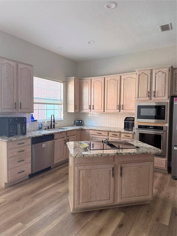 9709 Southern Hills Drive, Plano, TX 75025 Kitchen featuring light-tone wood cabinetry, stone countertops, a central island with a built-in cooktop, stainless steel appliances, and wood-finish flooring