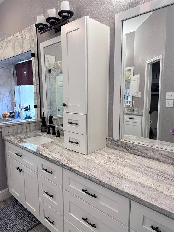 9709 Southern Hills Drive, Plano, TX 75025 Double vanity featuring white cabinetry, stone-surface countertops, integrated under-mount sinks, matte black hardware, and framed wall mirrors