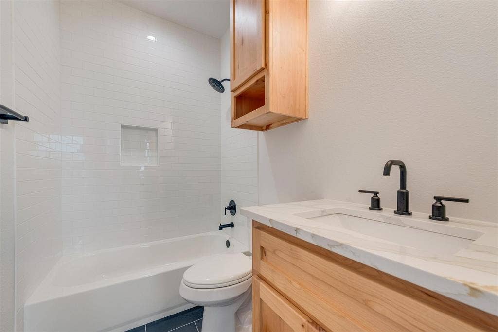 1001 Devoss Court, Caddo Mills, TX 75135 Bathroom featuring a wood-finish vanity with a stone-top integrated sink, matte black widespread faucet, subway tile shower surround with a built-in recessed niche, and matching wood-finish wall cabinetry