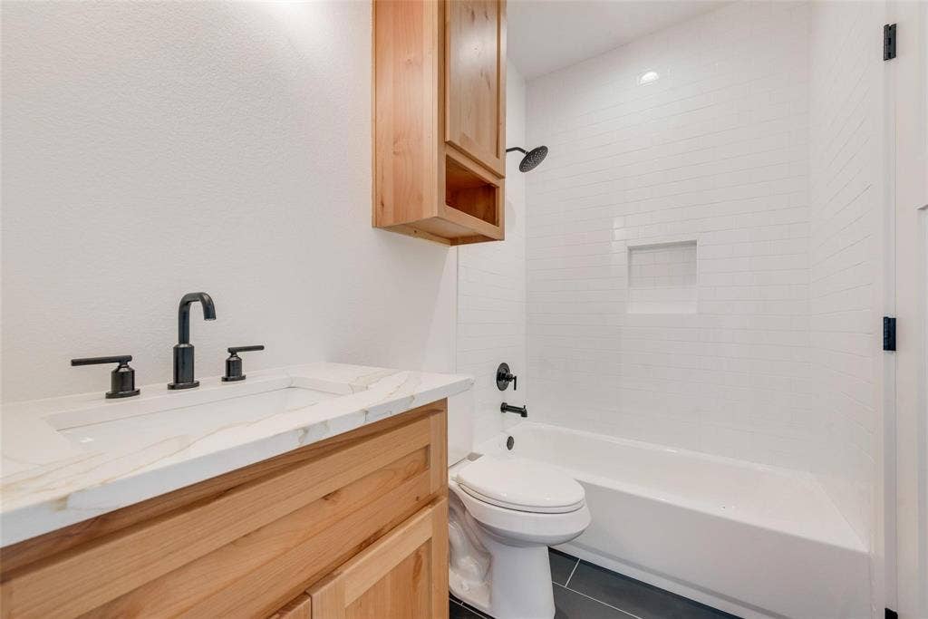 1001 Devoss Court, Caddo Mills, TX 75135 Natural wood vanity with stone-finish countertop, white subway tile shower surround with integrated niche, and matte black fixtures