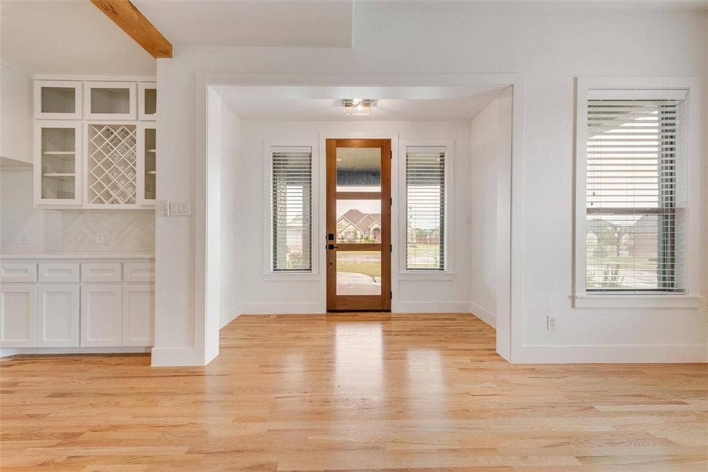 1001 Devoss Court, Caddo Mills, TX 75135 Wood-finish flooring, white cabinetry featuring built-in wine storage, and a natural wood-frame front door with glass panels