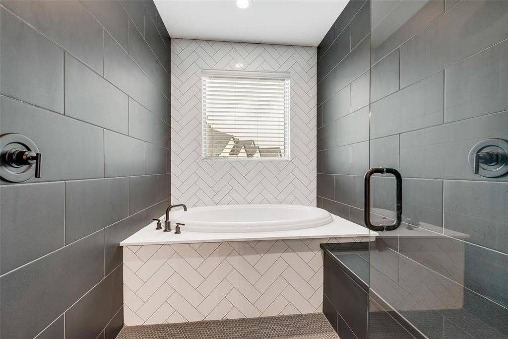1001 Devoss Court, Caddo Mills, TX 75135 Deep soaking tub with a white surround and herringbone-patterned tile inlay, contrasting matte black plumbing fixtures, and large-format dark wall tile