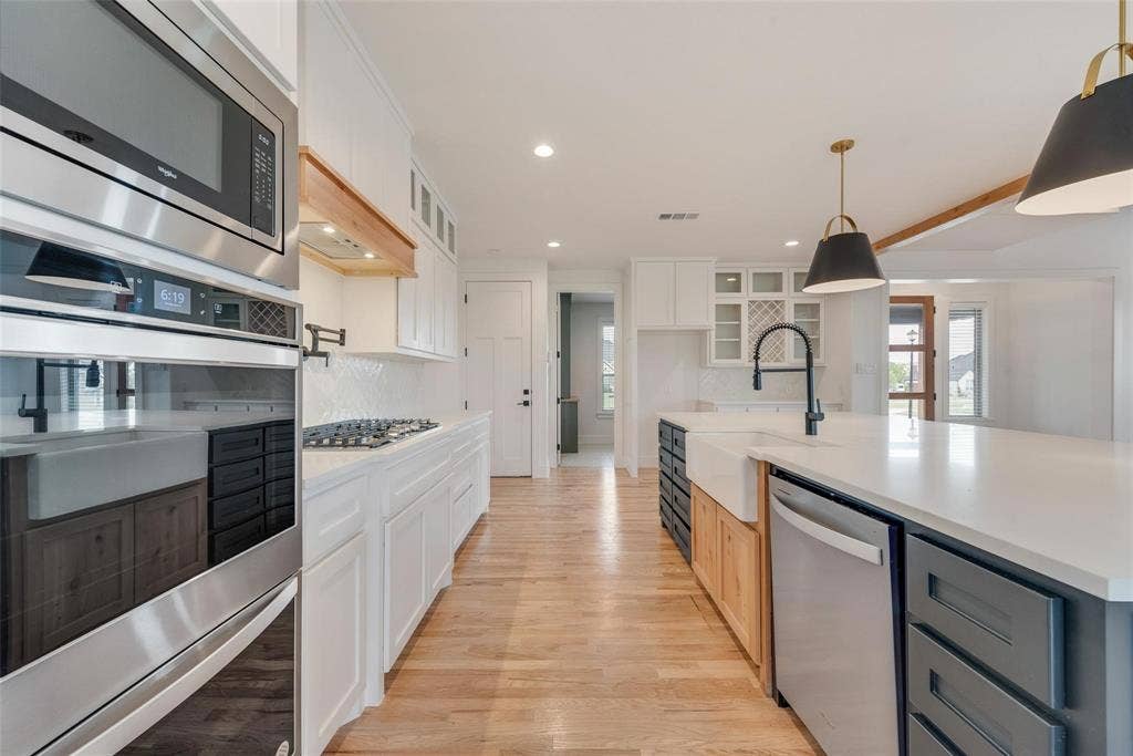 1001 Devoss Court, Caddo Mills, TX 75135 Kitchen featuring an expansive stone-surface island with a farmhouse sink, stainless steel wall-mounted oven and microwave, natural wood-finish flooring, white shaker-style cabinetry, and matte black pendant lighting