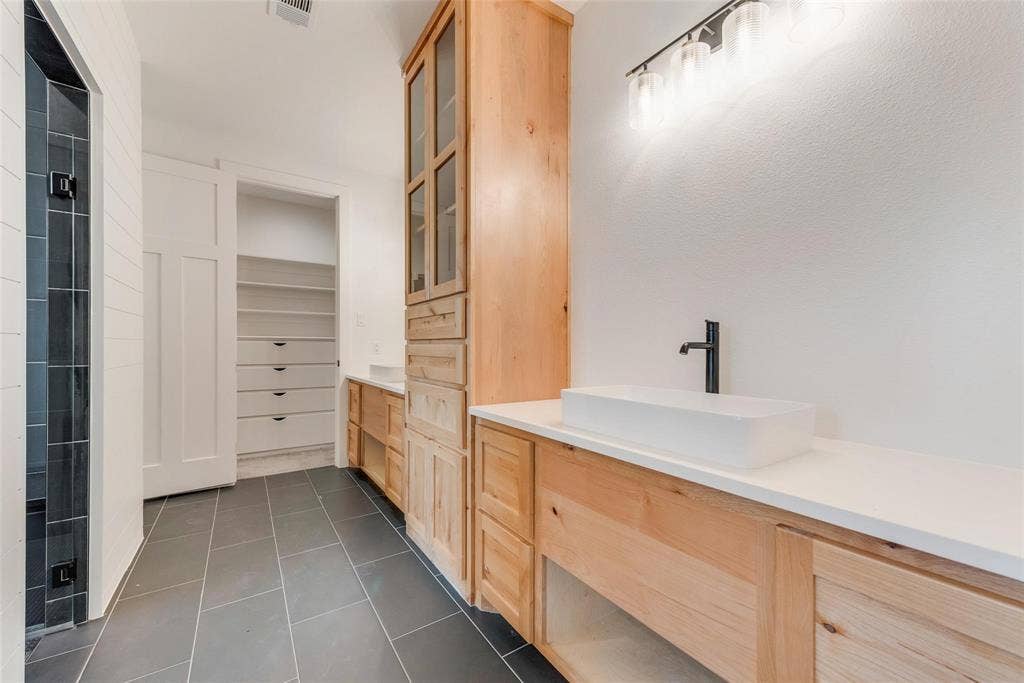 1001 Devoss Court, Caddo Mills, TX 75135 Custom wood cabinetry with an integrated tower, rectangular vessel sinks, light-toned solid surface countertops, matte black plumbing fixtures, and dark large-format tile flooring