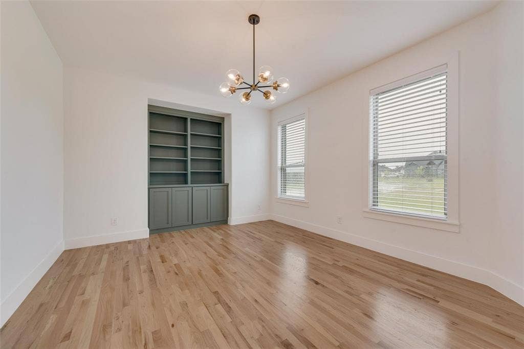 1001 Devoss Court, Caddo Mills, TX 75135 Room featuring wood-finish flooring, built-in floor-to-ceiling cabinetry, a multi-arm pendant light fixture, and two windows with horizontal blinds
