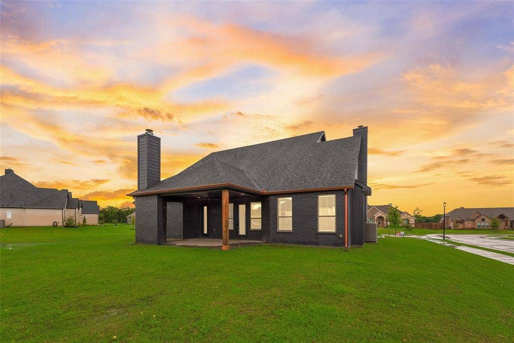 1001 Devoss Court, Caddo Mills, TX 75135 Dark exterior siding with a multi-gabled roofline, exterior brick chimneys, and a covered rear patio featuring wooden structural posts situated on a level lot