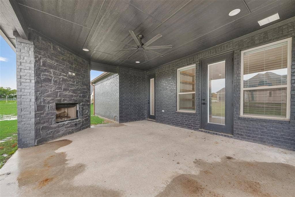1001 Devoss Court, Caddo Mills, TX 75135 Dark-toned brick exterior featuring a covered patio, dual chimneys, multi-gabled roofline, and an expansive lawn