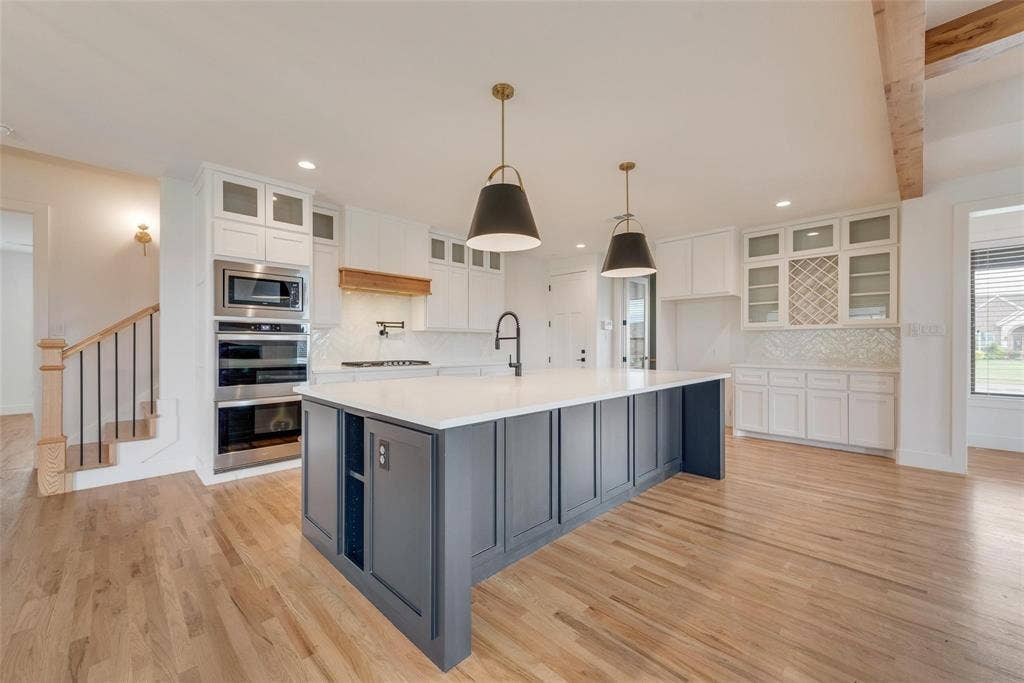 1001 Devoss Court, Caddo Mills, TX 75135 Kitchen featuring a central island with a solid surface countertop, two-toned cabinetry, built-in double wall ovens, glass-front upper cabinets with integrated wine storage, and wood-finish flooring