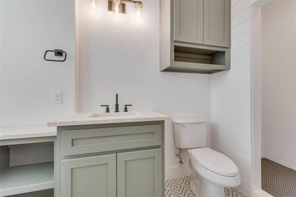 1001 Devoss Court, Caddo Mills, TX 75135 Shaker-style cabinetry, neutral-toned solid surface countertop, undermount sink with dark metallic hardware, wall-mounted cabinetry, and geometric patterned flooring