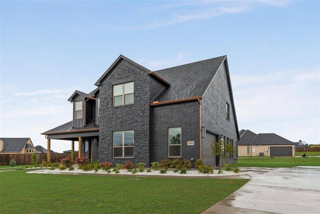 1001 Devoss Court, Caddo Mills, TX 75135 Two-story residence featuring a dark stone facade, multi-gabled roofline, covered porch, and concrete driveway