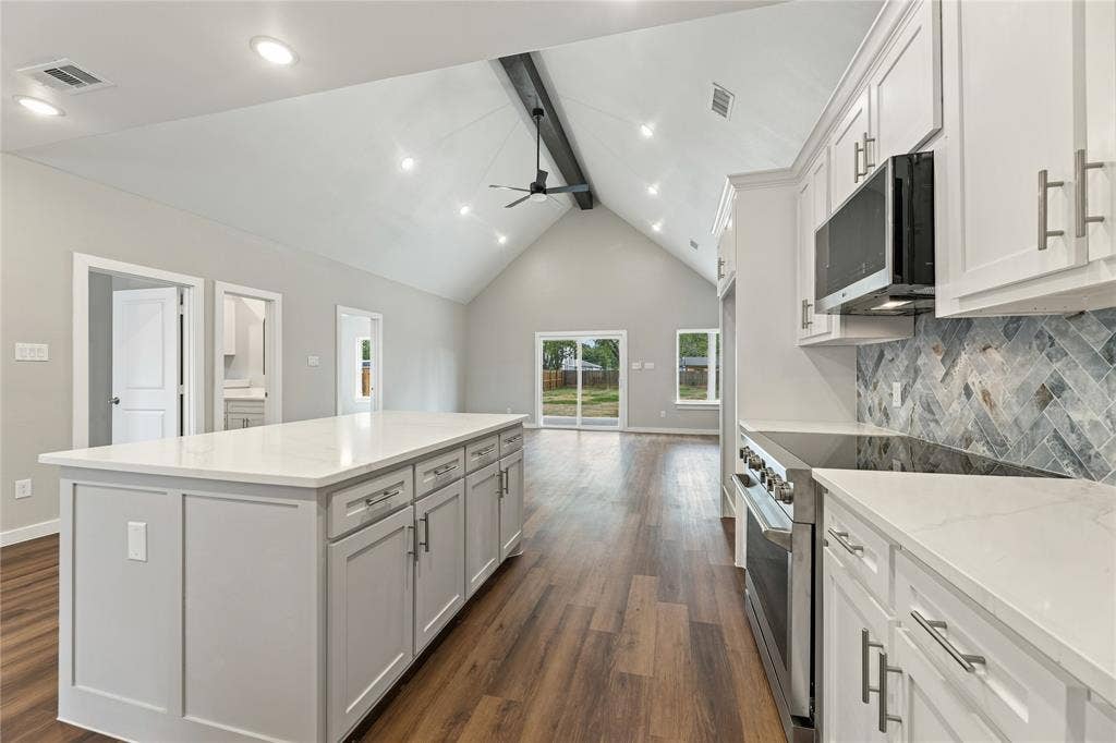 1242 Seminole Drive, Dallas, TX 75217 Kitchen featuring a vaulted ceiling with a decorative beam, central island with a quartz countertop, herringbone-patterned tile backsplash, stainless steel appliances, and wood-finish flooring