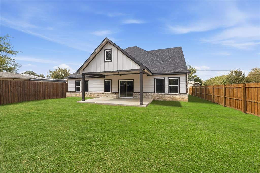 1242 Seminole Drive, Dallas, TX 75217 Rear exterior featuring a covered concrete patio, board-and-batten siding, stone masonry skirting, asphalt shingle roofing, and perimeter wood privacy fencing
