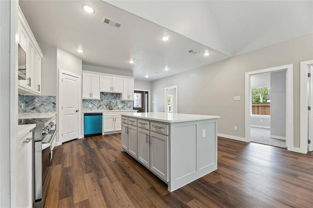 1242 Seminole Drive, Dallas, TX 75217 Kitchen featuring a central island with a solid surface countertop, white shaker-style cabinetry, a herringbone-patterned tile backsplash, stainless steel appliances, and wood-finish flooring