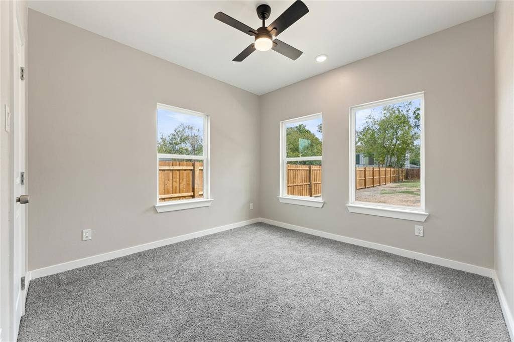 1242 Seminole Drive, Dallas, TX 75217 Neutral-toned interior featuring plush carpeting, three light-filled windows, and a matte black ceiling fan with integrated lighting