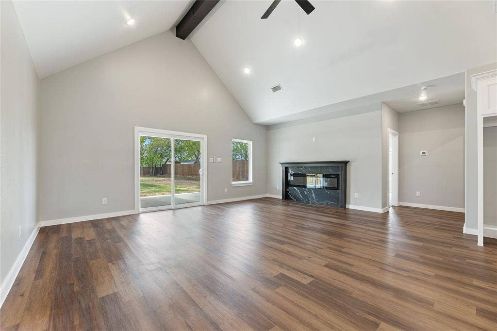 1242 Seminole Drive, Dallas, TX 75217 Vaulted ceiling with exposed beam, wood-finish flooring, fireplace with dark stone surround, and sliding glass door